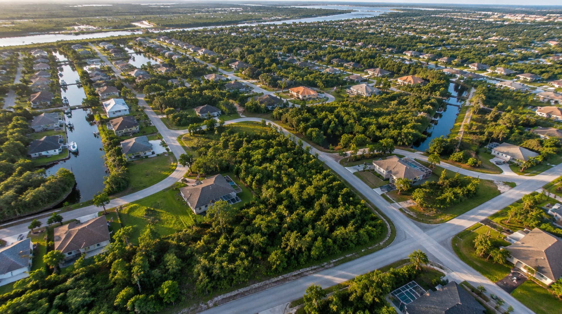Aerial view of a subdivision with finished homes, wooded vacant lots and canals